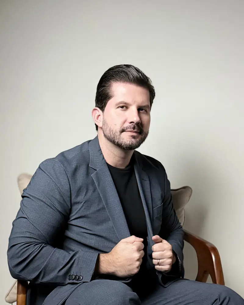 Dr. Joaquim Menezes sentado, ajeitando o blazer cinza, em estúdio de fundo claro